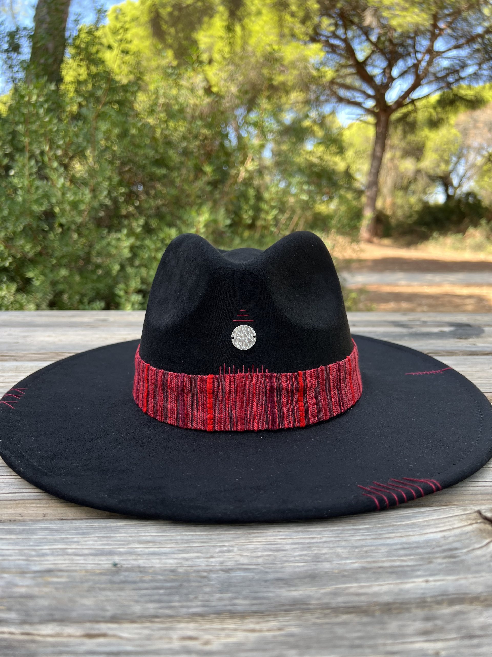 Sombrero negro artesanal Nature One of a Kind con cinta en tonos rojizos, bordados y dije plateado central.